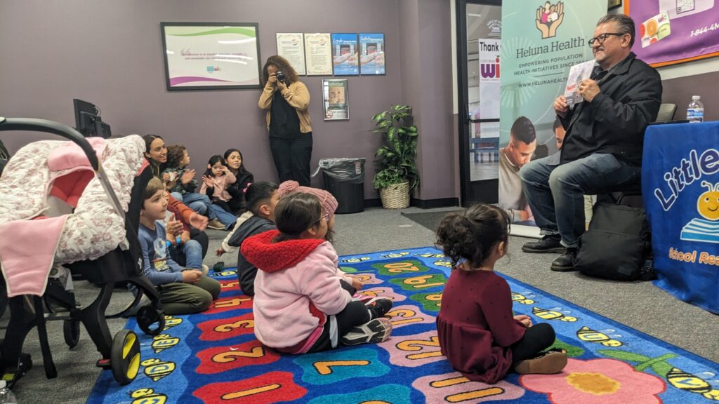 Artist and illustrator Lalo Alcaraz (far right) reads Poquita's Garden to children at a book launch event. Photo by Heluna Health.